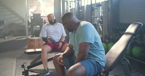 African american men resting and chatting after workout with shaker bottle on bench