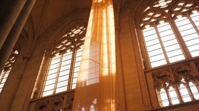Amber fabric filtering sunlight through gothic cathedral arched windows, casting shadows