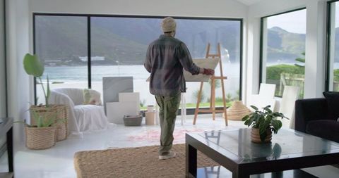 Indian artist painting on canvas in coastal minimalist living room studio with ocean view