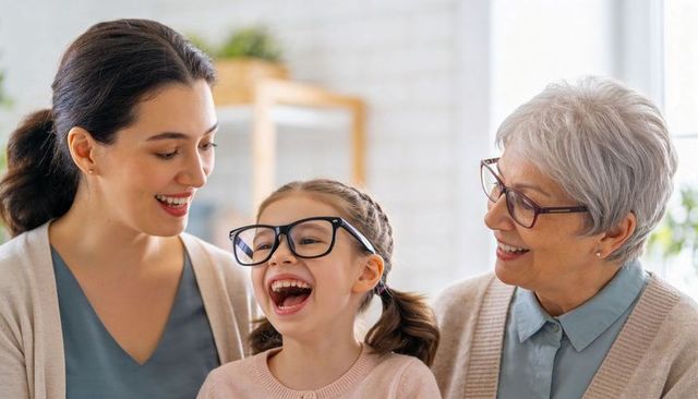 Multigenerational family laughing as child wears oversized glasses in sunlit living room