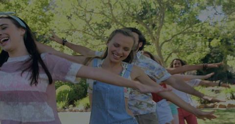 Friends walking single-file through sunny park laughing stretching arms playful summer fun