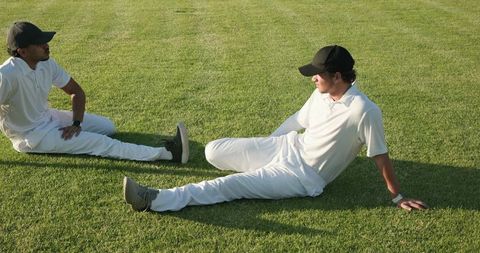 Resting Teammates on Sunlit Grass in White Uniforms and Black Caps