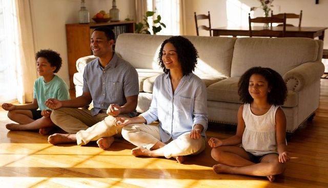 Family meditating together on sunlit hardwood floor in cozy living room