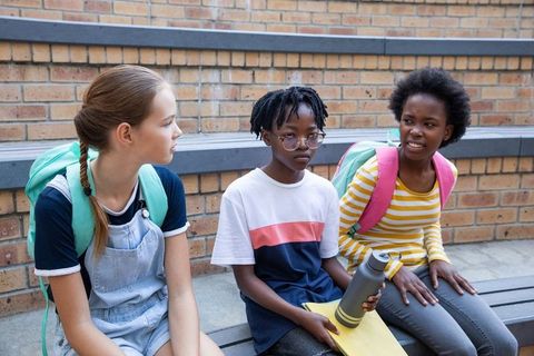 Diverse Students Sitting on Bleachers with Backpacks Discussing School Activities
