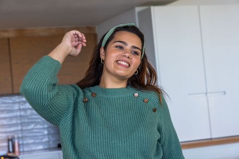Smiling young woman adjusting hair in modern kitchen wearing green sweater and headband