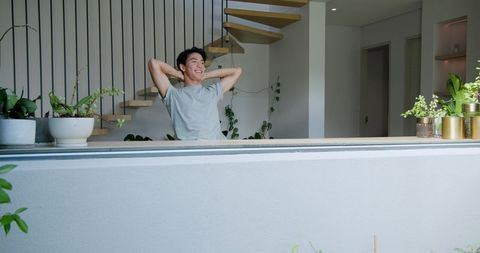 Asian Man Relaxing on Modern Balcony with Greenery