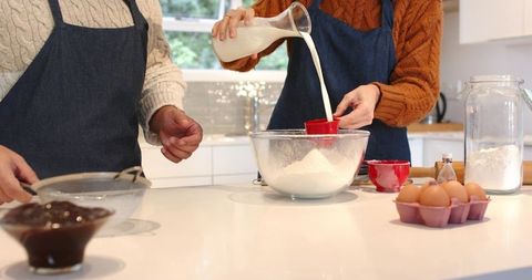 Couple baking together in bright modern kitchen pouring milk into flour for homemade cakes