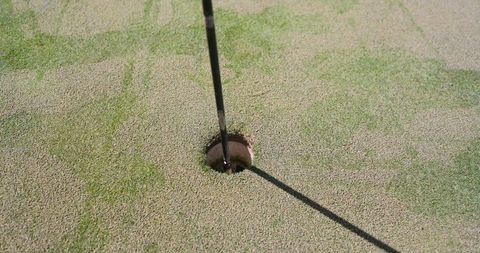Flagstick casting shadow on sunlit golf putting green