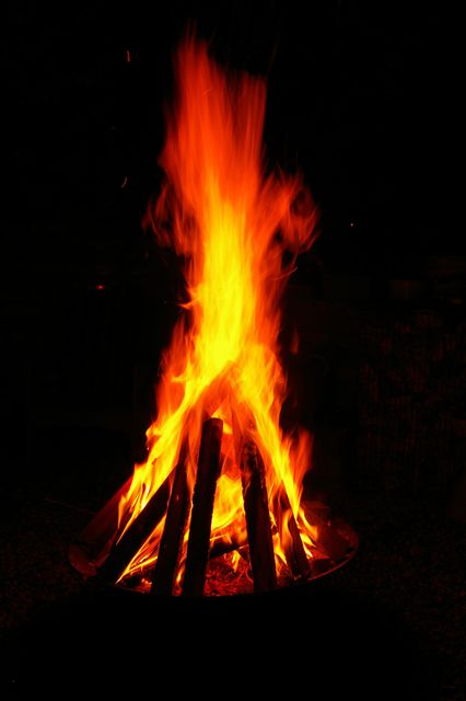 A bright campfire with tall, glowing flames projects warmth on a dark night. Can be used for camping themes, outdoor activities, warmth, or to evoke feelings of cozy gatherings around a bonfire.