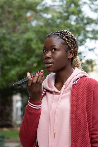 African American woman speaking into smartphone in park wearing pink hoodie red jacket