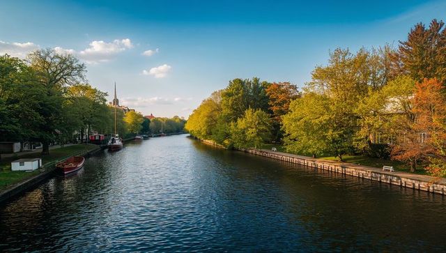 Flowing autumn canal promenade reflecting sky with moored sailboat
