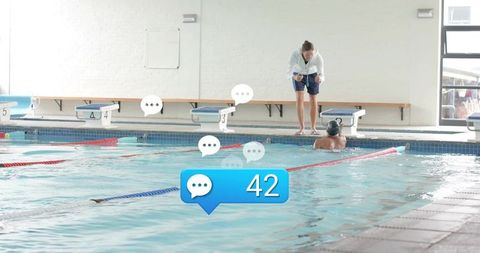 Female coach leaning poolside coaching swimmer during lap training with message notification bubble