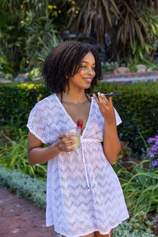 Young woman speaking into phone holding green smoothie with strawberry in backyard garden