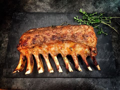Roasting rack of lamb on slate board with thyme garnish and charred bones