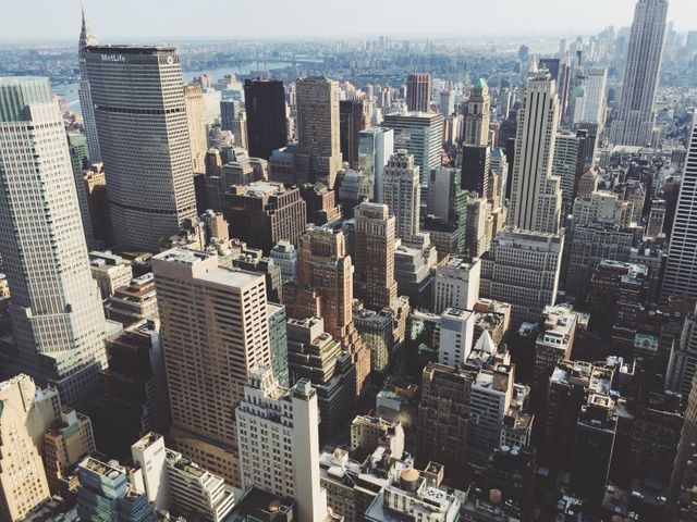 Aerial view of Manhattan's dense cluster of skyscrapers under sunny skies. This image highlights the bustling urban environment and iconic buildings. Ideal for use in articles, travel recommendations, real estate promotions, and business presentations showcasing New York City.