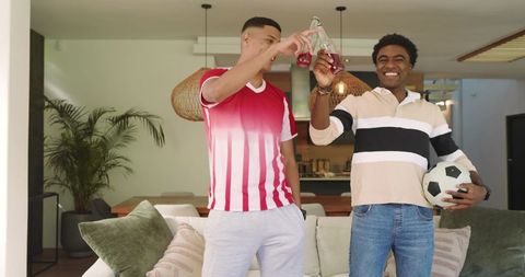 Diverse Friends Celebrating with Drinks and Soccer Ball in Living Room