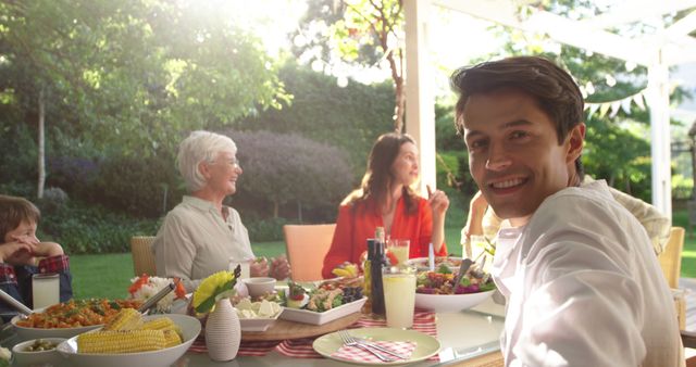 Family gathering in backyard garden, enjoying meal together with fresh salads, corn on the cob, beverages. Perfect for ads about family values, outdoor dining, summer events, social gatherings.