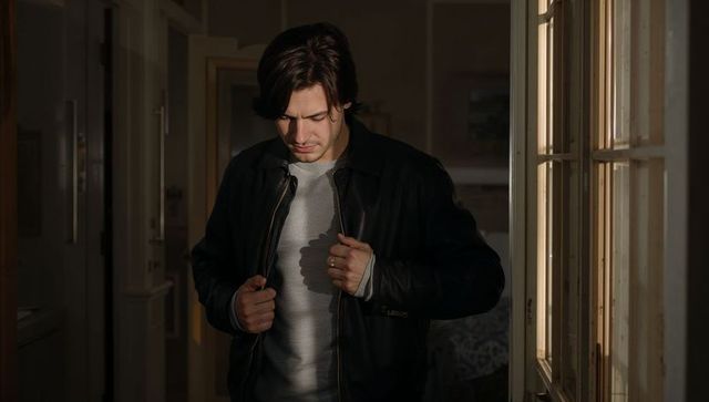 Man adjusting jacket zipper in dim hallway with warm window light casting shadow