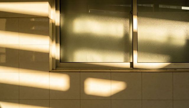Warm sunset light casting geometric shadows on frosted window and tiled wall