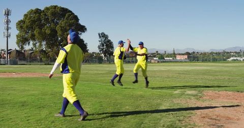 High-fiving baseball teammates celebrating catch in bright yellow uniforms on grassy outfield