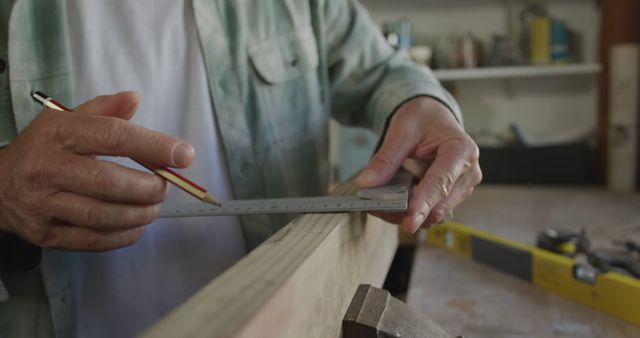Caucasian man marking wooden bar using pencil and ruler in workshop. Domestic life, lifestyle and free time, unaltered.