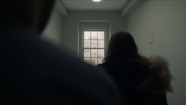 Silhouetted woman wearing fur hood standing in stairwell facing window with city view