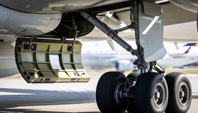 Aircraft main landing gear touching runway with open gear bay door and tire smoke closeup