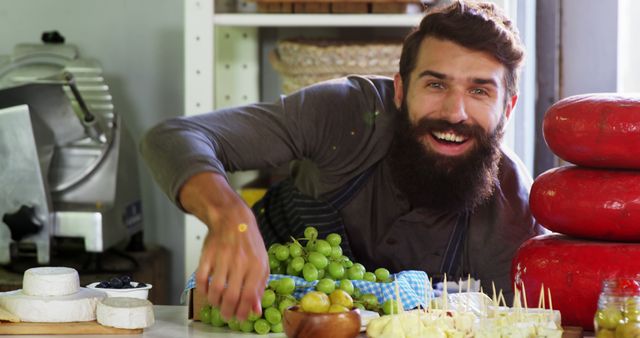 Cheerful Bearded Man Arranging Fresh Cheeses and Grapes in Delicatessen - Download Free Stock Images Pikwizard.com