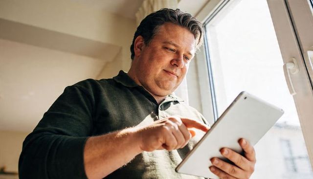 Middle-aged man using tablet near window in bright modern home interior