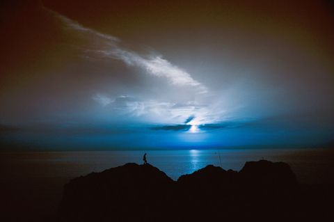 Lone Figure Stands on Cliff at Twilight Overlooking Ocean