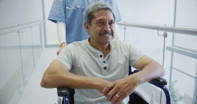 Senior biracial man in a wheelchair at a medical facility, with copy space. He shares a moment of optimism with a healthcare professional in the background.