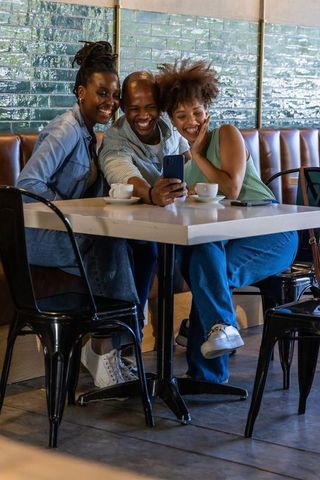 African american friends taking selfie and laughing at cozy cafe booth over coffee