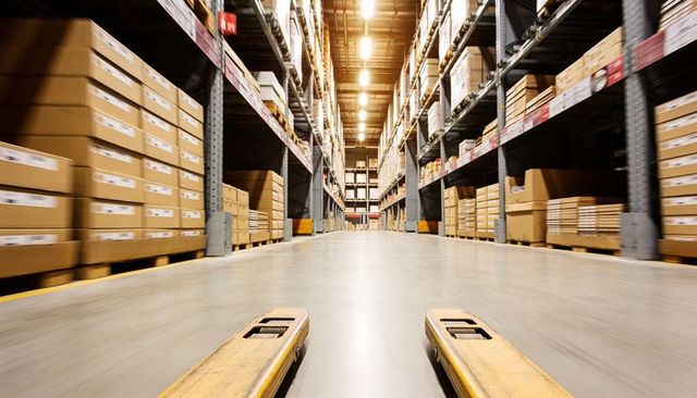 Low-angle pallet jack moving through high-bay warehouse aisle with stacked boxes