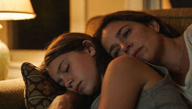 Mother and teen daughter cuddling and resting on sofa at night, intimate cozy moment
