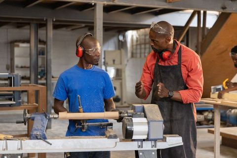 African american mentor mentoring apprentice turning wood lathe in workshop