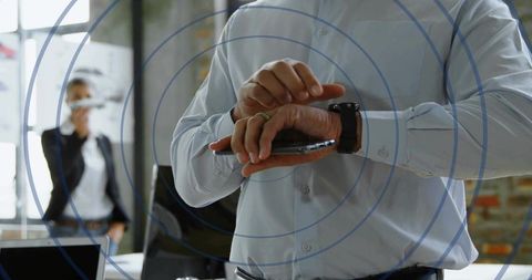 Businessman tapping smartwatch while holding smartphone in office with wireless rings