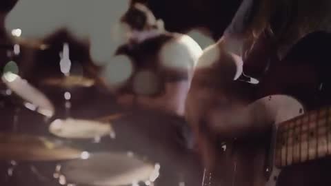 Guitarist playing close-up neck while drummer fades into bokeh, building live band energy