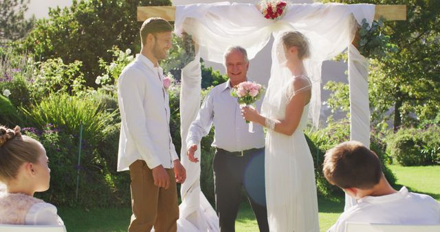 Caucasian bride and groom standing at outdoor altar with wedding officiant during ceremony. romantic summer wedding outdoors.