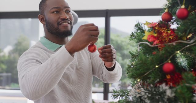 Man joyfully decorating a Christmas tree with red baubles inside a cozy home. This can be used for themes related to holiday preparations, family celebrations, festive decorations, and creating joyful Christmas memories.