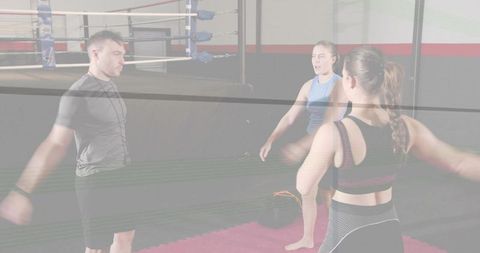 Boxing coach leading shoulder mobility warm-up with two women on red gym mat by ring