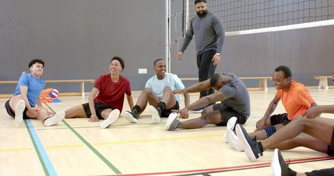 Multiracial male volleyball team stretching and laughing during indoor training session
