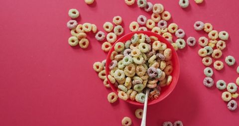 Colorful breakfast cereal in bowl with spoon on pink background