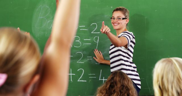 Smiling caucasian female teacher pointing to elementary schoolgirl with hand raised in maths class. Education, childhood, teaching, learning, school and work, unaltered.