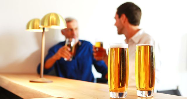 Men chatting and drinking beer in a modern bar with contemporary gold lighting. This could be used in advertising for bars, pubs, or social venues, promotions for beer and drink brands, or articles and blogs about nightlife, socializing, and friendship.