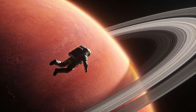Astronaut floating above orange ringed planet with dramatic sweeping rings and orbit