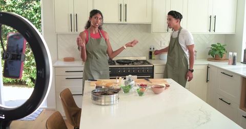 African American hosts filming cooking tutorial in modern kitchen with marble island and ring light