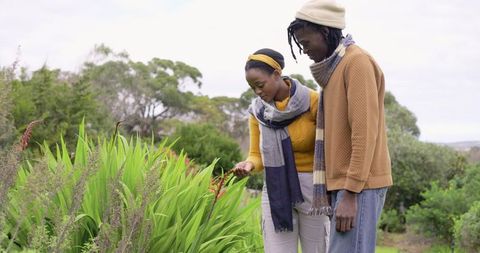 African American Couple Exploring Garden Touching Red Blooms Wearing Scarves and Beanie