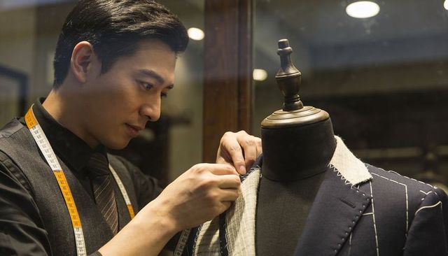 Tailor adjusting bespoke pinstripe suit on mannequin, measuring tape showing precision