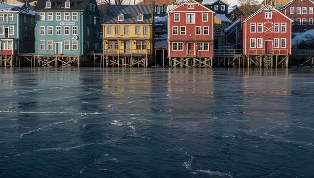 Colorful boathouses lining frozen harbor reflecting on ice with wooden stilts and pilings