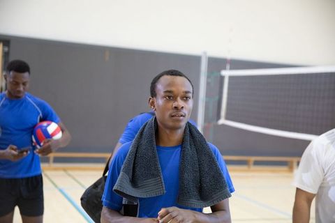 African american volleyball player standing on indoor court holding towel and ball